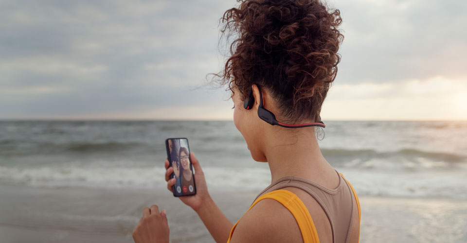 Športnik sprejema klic na plaži, medtem ko uporablja slušalke s kostnim prevodom