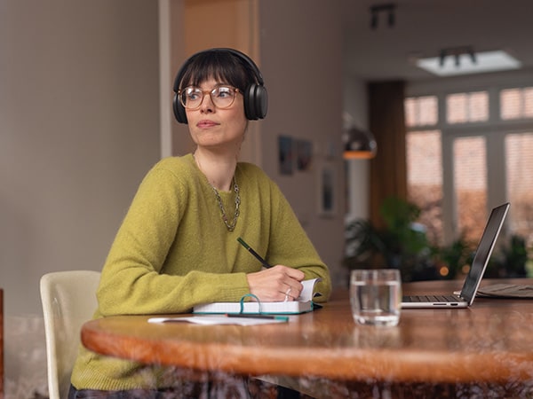 Oseba, ki nosi udobne Philipsove slušalke, sedi za mizo s beležko in prenosnikom