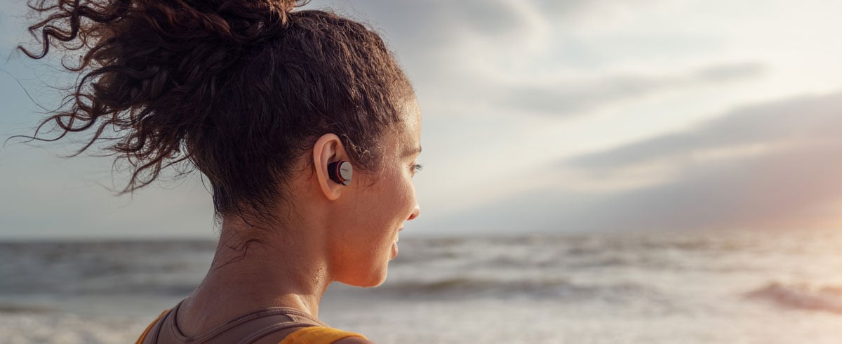 Ženska s popolnoma brezžičnimi slušalkami na obali