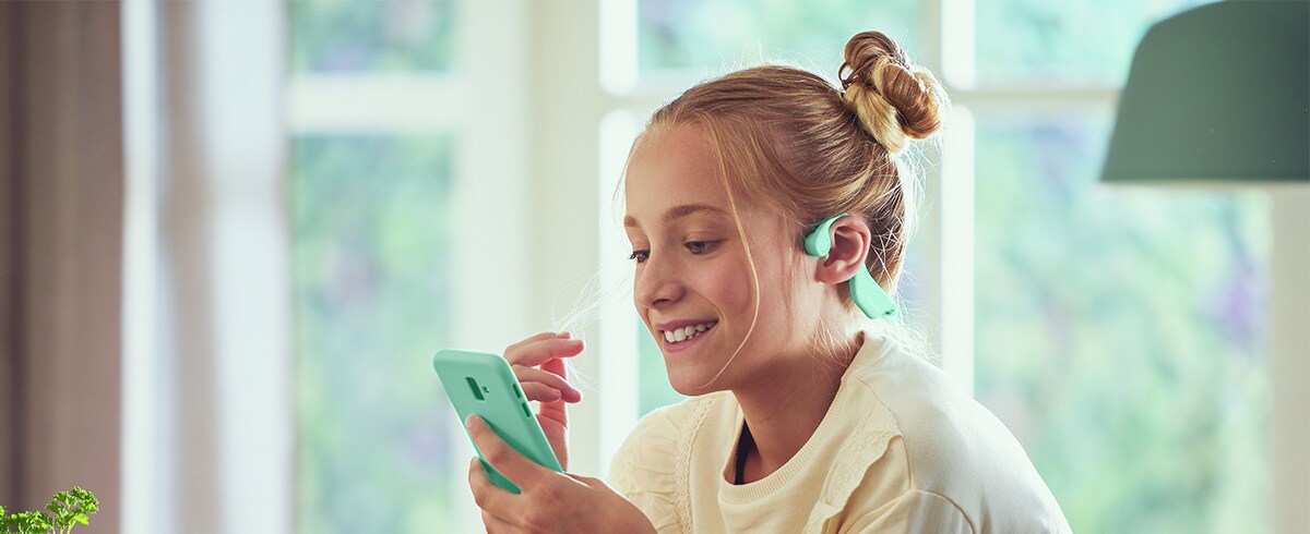 Deklica uporablja zelene kostnoprevodne otroške slušalke