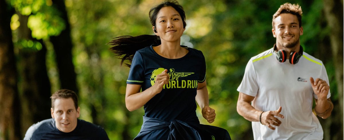 Trije udeleženci teka Wings for Life World Run veselo tečejo z nadetimi športnimi slušalkami Philips.