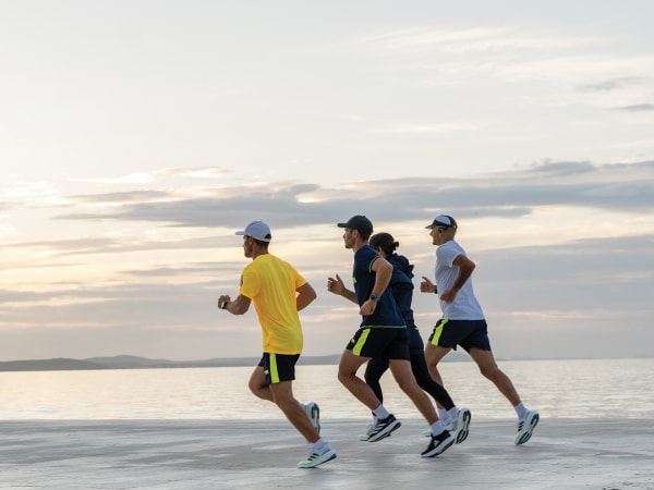 Štirje udeleženci teka skupaj tečejo na plaži.